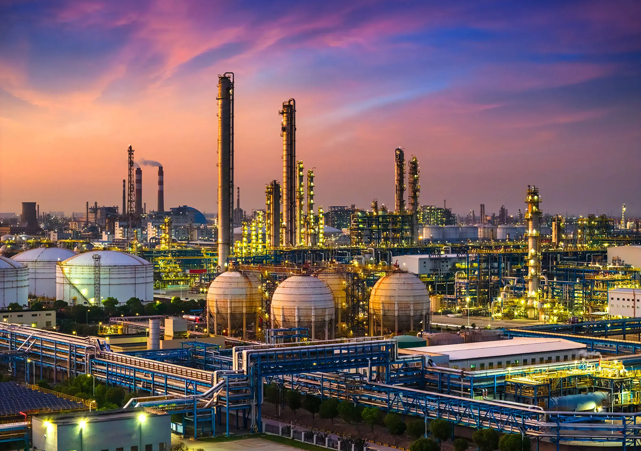 Industrial refinery complex under a colorful sunset sky.